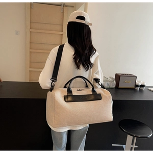 Detail of a large beige canvas travel bag with black leather straps on a model back