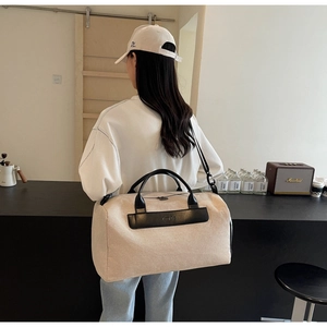 Detail of a large beige canvas travel tote with black leather straps in a cafe setting