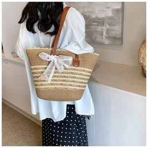 Detailed close-up of straw tote bag with white lace bow and brown leather shoulder strap