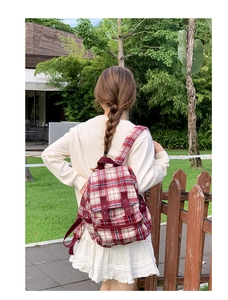 Outdoor shot of a red and white checkered backpack with adjustable drawstring and gold accents
