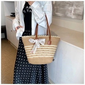 Detail view of woven straw tote bag with brown leather handles and white lace bow accessory