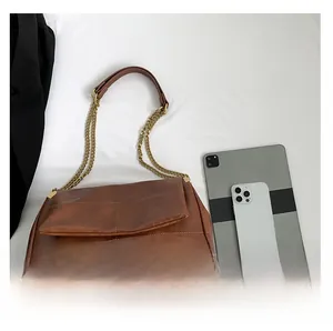 Detailed top view of brown PU leather crossbody bag with chain strap on white fabric