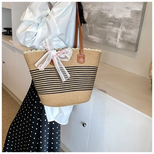 Detail of woven straw tote bag featuring pink floral lace bow and slim brown leather straps