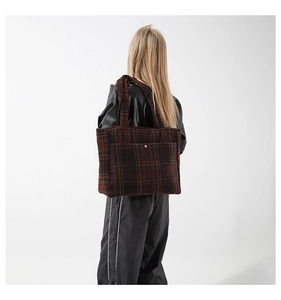 Détail d'un grand sac cabas à carreaux en laine avec bouton pression doré porté à l'épaule