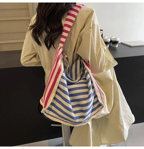 Detail of a large capacity blue and white striped canvas hobo bag with red straps