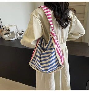 Detail shot of canvas tote bag with blue and pink stripes on a model in a cafe setting