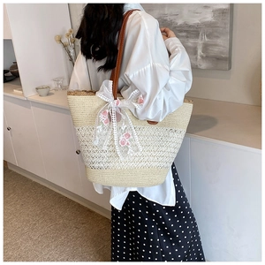 Detailed close-up of straw tote bag with lace bow and floral embroidery on shoulder strap
