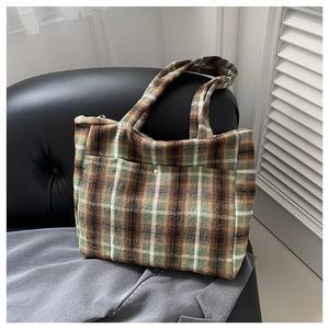 Sac cabas à carreaux vert et marron en laine avec boucle dorée sur un siège