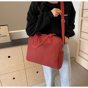 Detailed macro view of a red canvas tote bag with adjustable wide strap and front embossed text