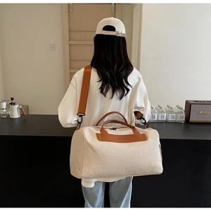 Detail of canvas travel bag featuring orange leather trim and adjustable nylon strap