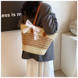Detail of a large straw tote bag featuring a white floral lace bow and leather straps