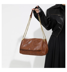 Detail of a brown oil wax leather crossbody bag featuring gold chain and cross stitching