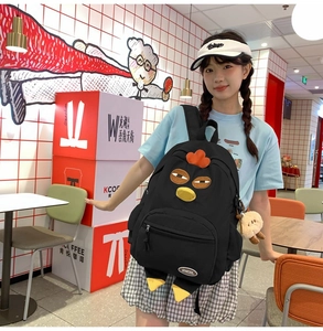 Detail of a black nylon backpack with a fun chicken design and plush sheep pendant