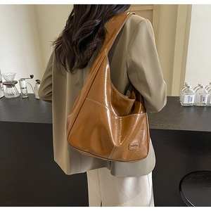 Close-up of a brown glossy patent leather tote bag with FASHION label and stitching
