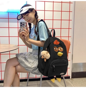 Detail shot of black nylon backpack featuring a cartoon chicken face and plush pendant