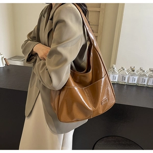 Detailed view of brown PU leather tote bag with white contrast stitching and logo on model