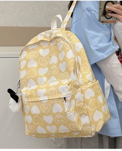 Detail of yellow nylon backpack featuring white heart cartoon prints and plush puppy charm
