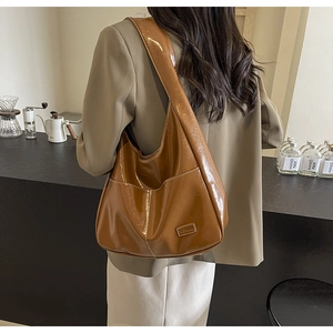 Detail of glossy brown PU leather hobo bag with a metallic shine on a model's shoulder