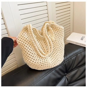 Fashionable cream woven mesh tote bag with fringe details on a black leather sofa