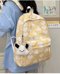 Detail of yellow nylon backpack featuring cartoon prints and a cute plush puppy charm pendant