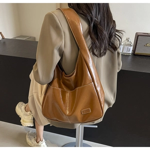 Detail of a brown PU leather hobo bag with a wide strap and fashion label on the front