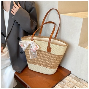 Detail of straw woven tote bag featuring floral embroidered bow and leather handles