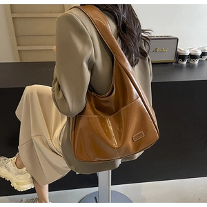 Detail view of large dark brown patent leather tote bag with glossy finish and metal tag
