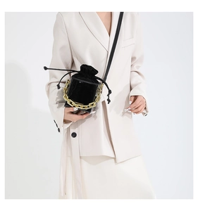 Mini borsa a secchiello nera con catena dorata indossata su un abito beige