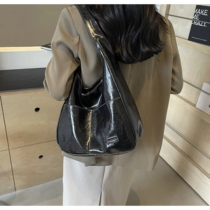 Detail view of black glossy PU leather tote bag featuring a Fashion metal label detail
