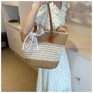 Detailed close-up of straw woven tote bag featuring white hollow crochet and leather handles