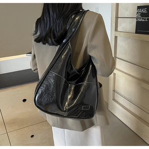 Close-up of black glossy PU leather shoulder bag with white contrast stitching and logo patch