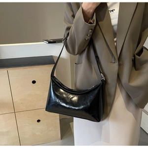 Detail of a black patent leather hobo bag with glossy finish and modern buckle strap
