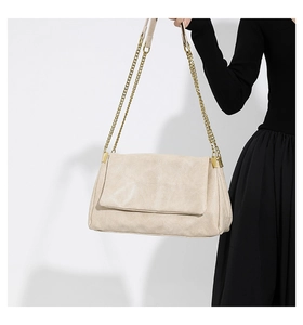 Detail of the cream-colored PU leather texture and golden metal chain strap on handbag