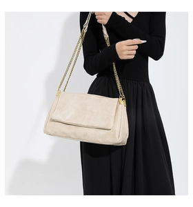 Detail of elegant beige PU leather handbag with luxury gold chain strap on black dress