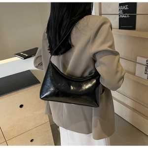 Close-up of black glossy PU leather underarm bag styled with a khaki blazer on model