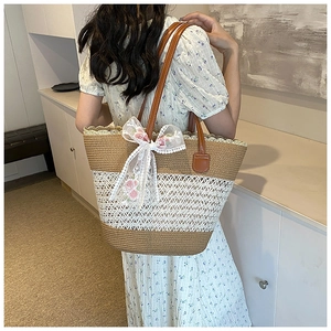 Detail of a woven straw shoulder bag with white lace floral accents and a silk scarf bow