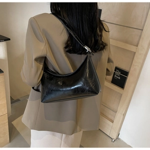Close-up of a stylish black glossy PU leather shoulder bag worn by a model in a minimal setting