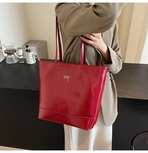 Detail of glossy deep red PU leather tote bag with a minimalist silver metal bow charm