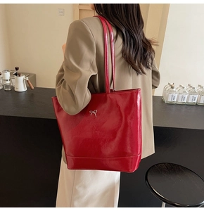 Deep red glossy patent leather tote bag with silver bow detail in a lifestyle cafe setting
