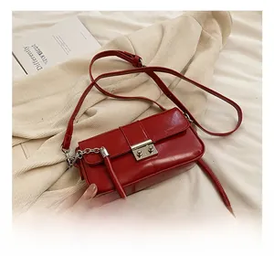 Detail of red patent leather crossbody bag featuring a polished metal buckle closure