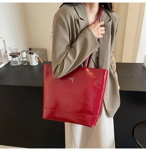 Close-up of a glossy red PU leather tote bag with a silver bow detail on a shoulder strap