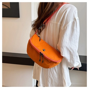 Detail view of the orange crossbody bag with black dual zippers and adjustable strap