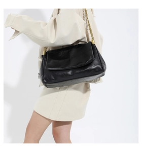 Close-up of black quilted leather handbag with gold chunky chain strap on a model