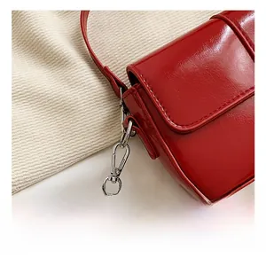Detail of red patent leather handbag featuring silver metal hooks and premium stitching