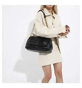 Detail of black quilted PU leather handbag with chunky gold chain strap on model