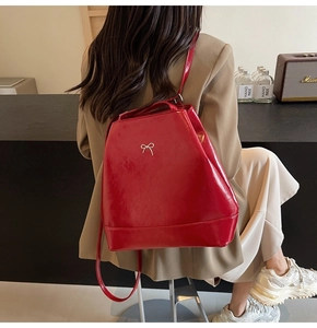 Detail view of glossy red PU leather backpack with a silver bow buckle and thin straps