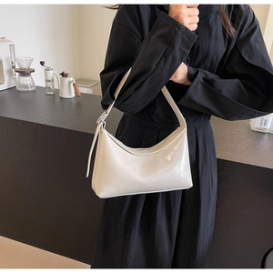 Detail of a white glossy faux leather hobo bag worn by a model in a minimal setting