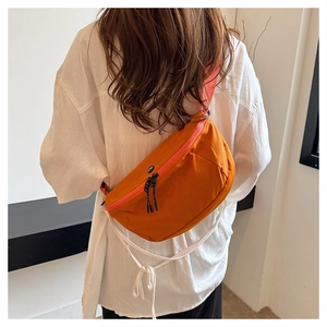 Detail view of a bright orange nylon crossbody bag worn over a white casual shirt