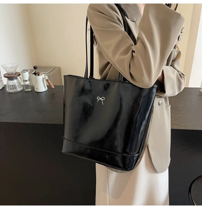 Detail of glossy black PU leather tote bag with silver bow buckle and shoulder straps