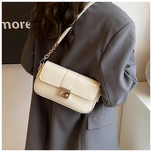 Detail of a creamy white PU leather crossbody bag with silver lock on a grey suit jacket
